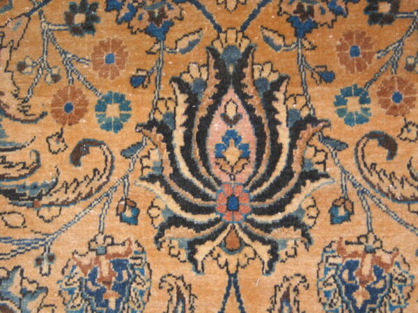 Intricate floral and vine pattern rug detail in shades of ochre, navy blue, black, and light brown.