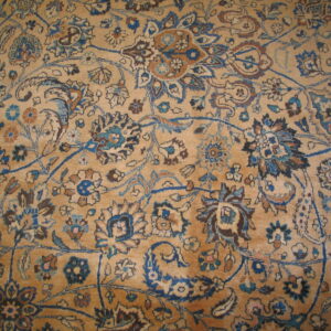 Detailed view of a tan rug featuring an intricate floral pattern in shades of blue and brown.