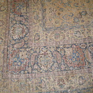 Low-pile rug with a faded tan ground, ornate blue, red, and pink patterns on a wood floor.