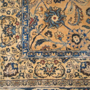 Close-up showing a tan rug field with detailed blue and brown traditional floral medallions and borders.