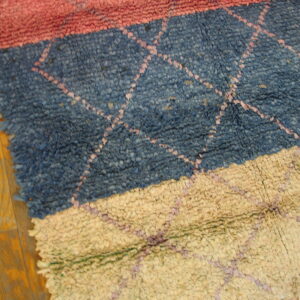 Coarse looped rug with pink, blue, and tan horizontal stripes and a subtle diamond pattern on hardwood.