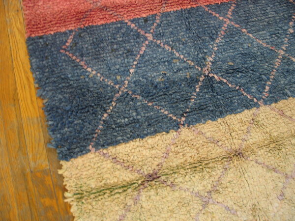 Coarse looped rug with pink, blue, and tan horizontal stripes and a subtle diamond pattern on hardwood.