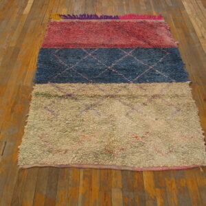 Multicolored striped rug in reddish-pink, navy blue, and cream sits on a rustic plank wood floor.