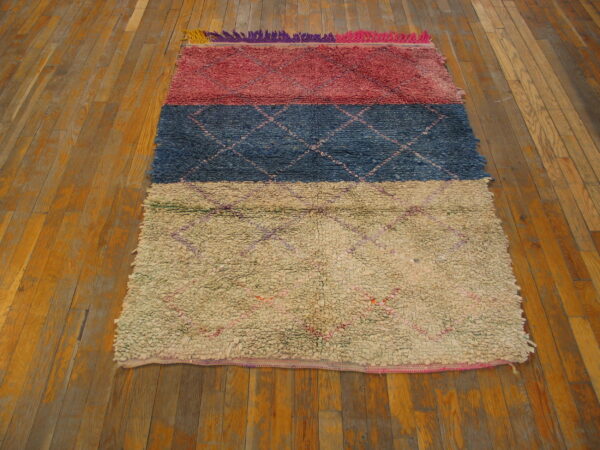 Multicolored striped rug in reddish-pink, navy blue, and cream sits on a rustic plank wood floor.