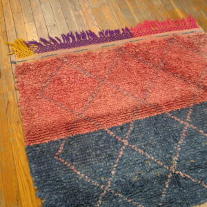 Chunky pink and blue color-block rug with subtle diamond pattern and multicolor fringe on wood flooring.