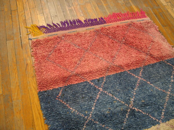 Chunky pink and blue color-block rug with subtle diamond pattern and multicolor fringe on wood flooring.