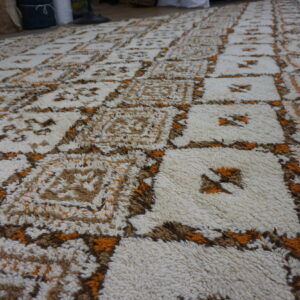 Shaggy cream rug with a geometric grid pattern in brown and bright orange colors.