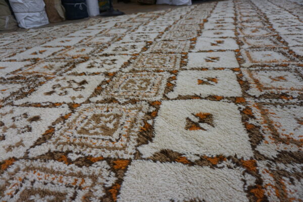 Shaggy cream rug with a geometric grid pattern in brown and bright orange colors.