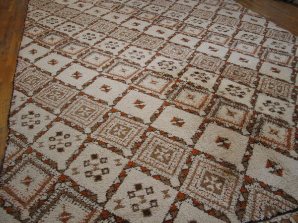 Off-white shaggy rug with brown and orange geometric diamond motifs rests on light brown wood flooring.