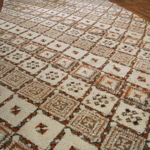A textured, shaggy rug with cream, brown, and orange geometric diamonds rests on hardwood flooring.