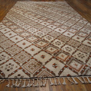 Cream high-pile rug with geometric brown and orange diamond patterns, featuring braided tassels on wood flooring.