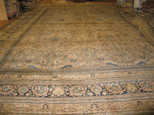 Oversize low-pile rug featuring intricate blue and beige floral patterns is displayed on wood flooring.