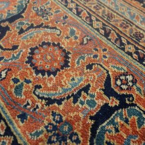 Close-up of a low-pile rug featuring ornate patterns in rust orange, navy, and teal blue.