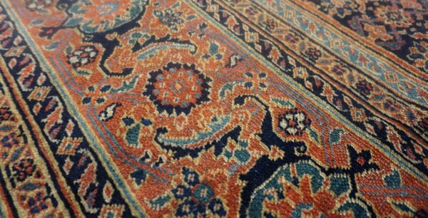 Close-up of a low-pile rug featuring ornate patterns in rust orange, navy, and teal blue.
