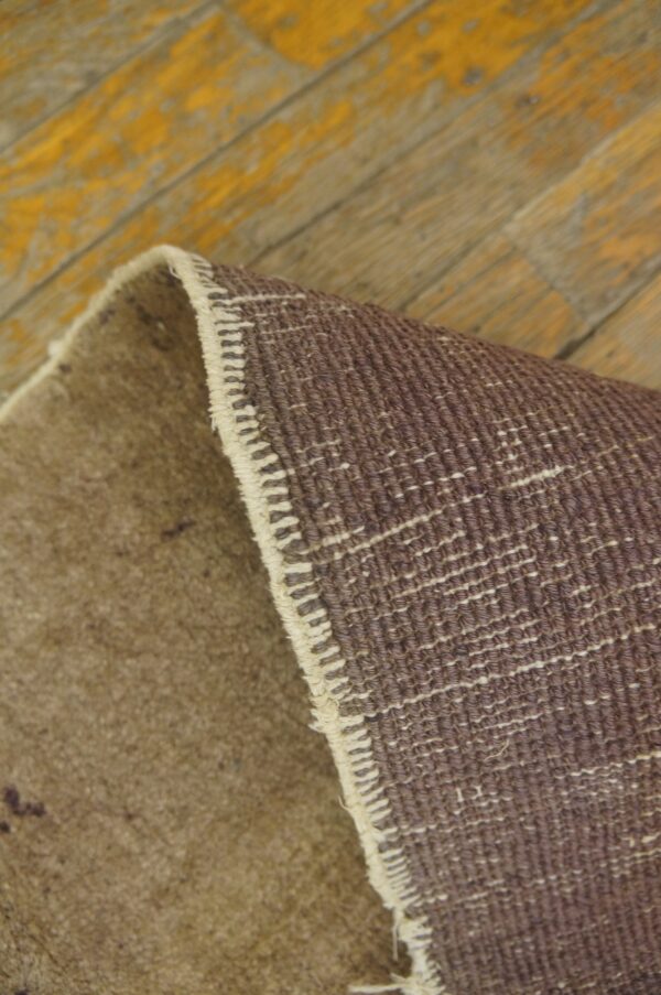 A brown rug is curled up revealing its dark woven backing on worn yellow painted wood planks.