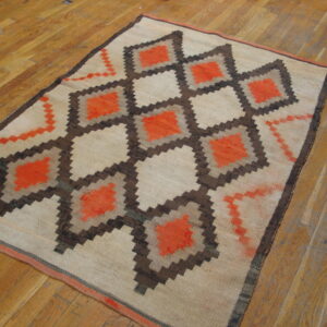 Geometric flatweave rug with repeating stepped diamonds in bright orange, brown, and tan on hardwood flooring.