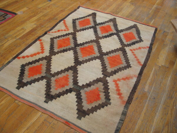 Geometric flatweave rug with repeating stepped diamonds in bright orange, brown, and tan on hardwood flooring.