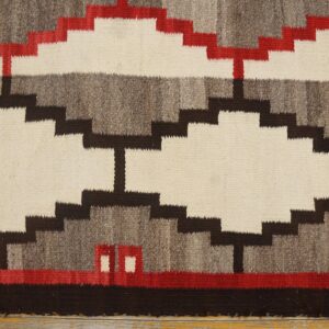 Stepped geometric rug in cream, gray, brown, and red laid on distressed natural wood flooring.
