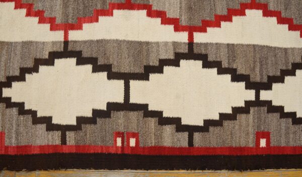 Stepped geometric rug in cream, gray, brown, and red laid on distressed natural wood flooring.