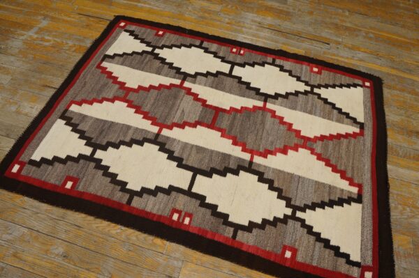 Geometric flatweave rug in cream, gray, red, and brown on distressed yellow-toned wood flooring.