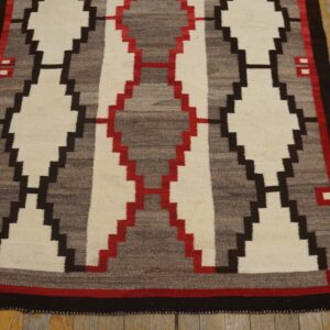 Flat-woven rug with stepped diamond patterns in cream, gray, red, and dark brown on old wood flooring.