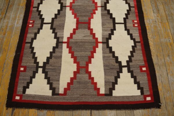 Flat-woven rug with stepped diamond patterns in cream, gray, red, and dark brown on old wood flooring.