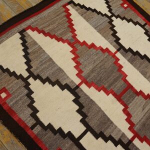 Geometric flatweave rug in cream, gray, dark brown, and red on distressed yellow wood floorboards.
