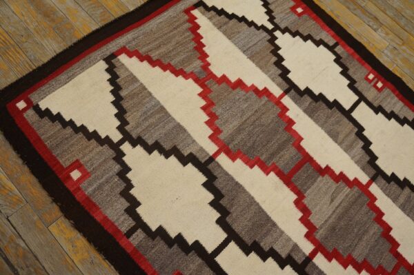 Geometric flatweave rug in cream, gray, dark brown, and red on distressed yellow wood floorboards.