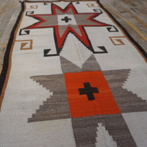 Geometric runner rug with star motifs in white, orange, brown, and black on distressed wooden plank flooring.