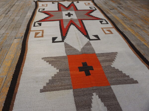 Geometric runner rug with star motifs in white, orange, brown, and black on distressed wooden plank flooring.