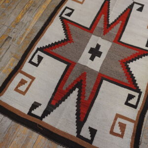Geometric rug with a central red and black star, corner key motifs, set on worn wood floors.