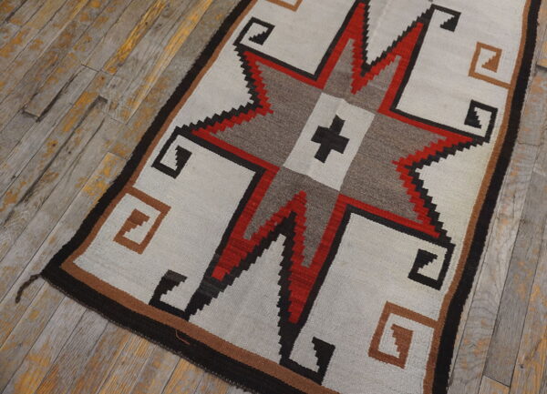 Geometric rug with a central red and black star, corner key motifs, set on worn wood floors.