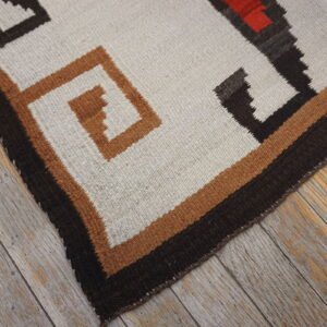 White, black, and rust geometric flatweave rug lying on distressed gray wood flooring.