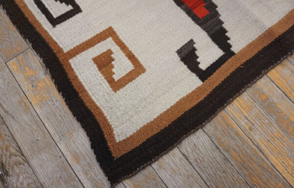White, black, and rust geometric flatweave rug lying on distressed gray wood flooring.