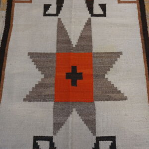 Flatweave runner rug with a gray, brown, and orange geometric star pattern on distressed wood floors.