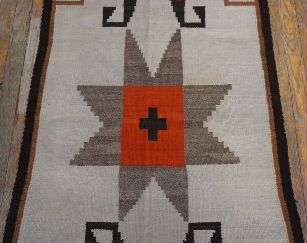 Flatweave runner rug with a gray, brown, and orange geometric star pattern on distressed wood floors.