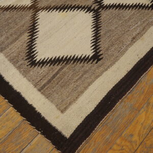 Geometric rug in natural brown, cream, and dark brown with a sawtooth pattern rests on worn wood planks.