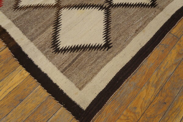 Geometric rug in natural brown, cream, and dark brown with a sawtooth pattern rests on worn wood planks.