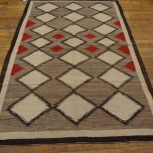 Geometric flatweave rug in cream, red, and brown diamond patterns laid on plank wood flooring.
