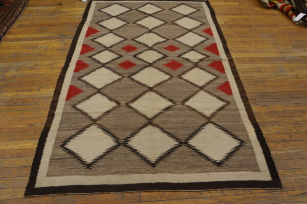 Geometric flatweave rug in cream, red, and brown diamond patterns laid on plank wood flooring.
