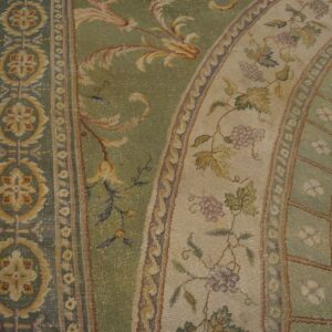 Ornate sage green and gold rug with detailed grapevine and floral borders rests on light wood flooring.