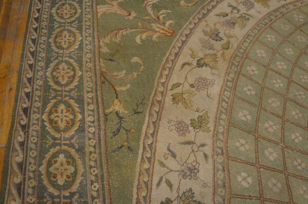 Ornate sage green and gold rug with detailed grapevine and floral borders rests on light wood flooring.