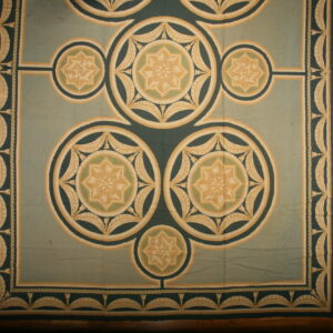 Sage and dark green rug with geometric medallions and stars, featuring tan accents on a hardwood floor.