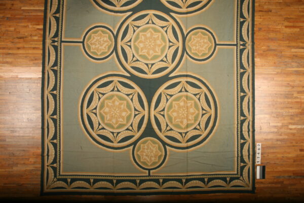 Sage and dark green rug with geometric medallions and stars, featuring tan accents on a hardwood floor.