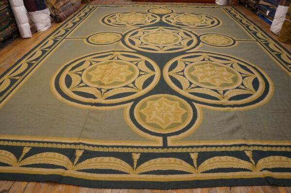 Large sage and dark teal rug with repeating yellow medallion and floral star patterns on wood floor.