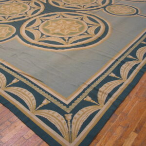 Low-pile rug in pale blue, teal, and gold with neoclassical medallions and leaf borders on wood planks.