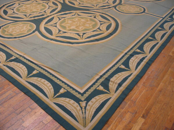 Low-pile rug in pale blue, teal, and gold with neoclassical medallions and leaf borders on wood planks.