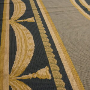 A flat, textured rug featuring teal, pale yellow, and sage botanical patterns rests on hardwood flooring.