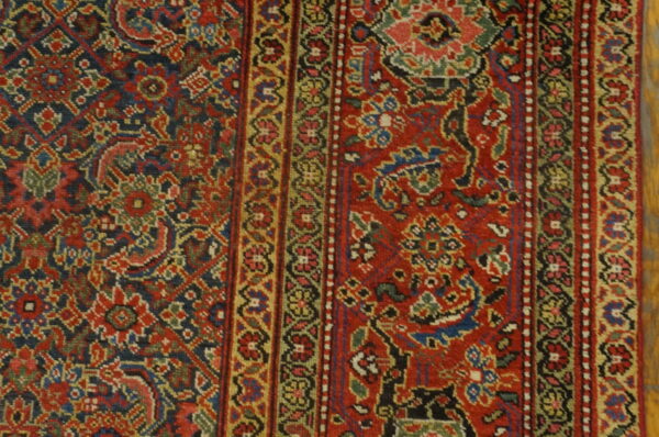 Detailed view of a low-pile rug featuring red, blue, and green ornate patterns with multiple guard borders.