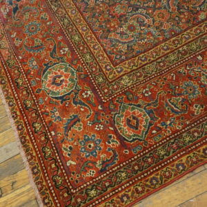 Ornate red and blue patterned rug with complex borders lying diagonally on rustic hardwood floors.